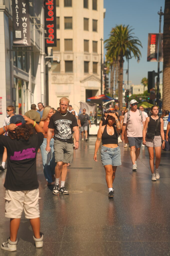Man in a black graphic tee walking past Hollywood Boulevard crowds, Los Angeles street scene.