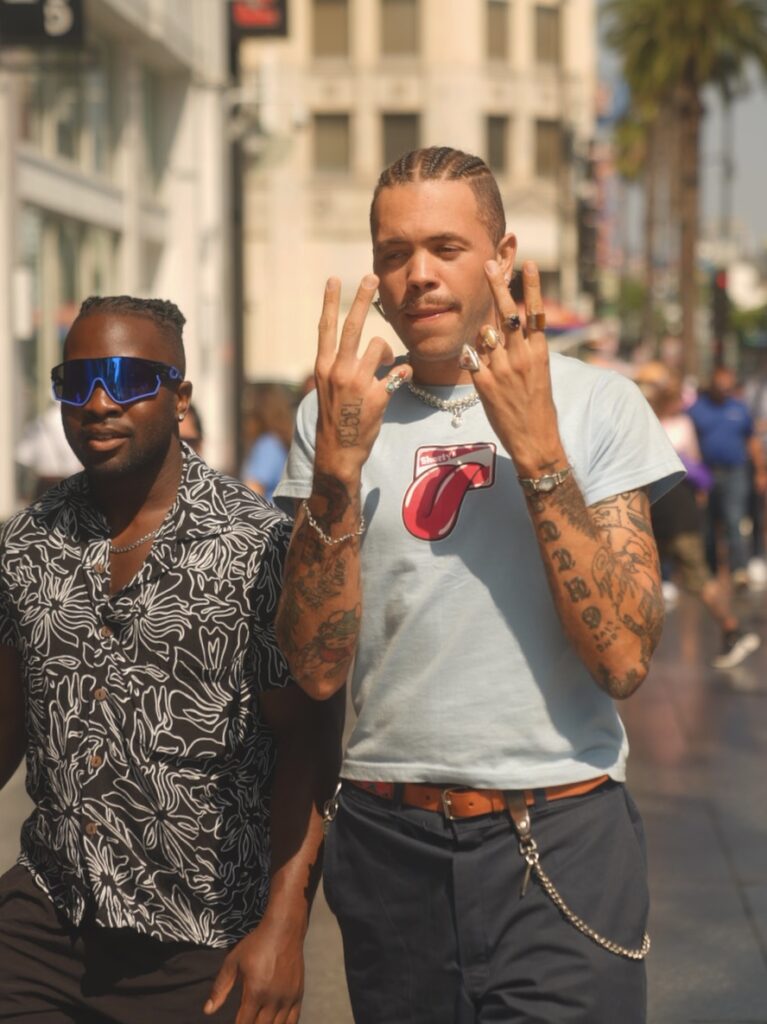 Tattooed man flashing hand signs while walking in Hollywood