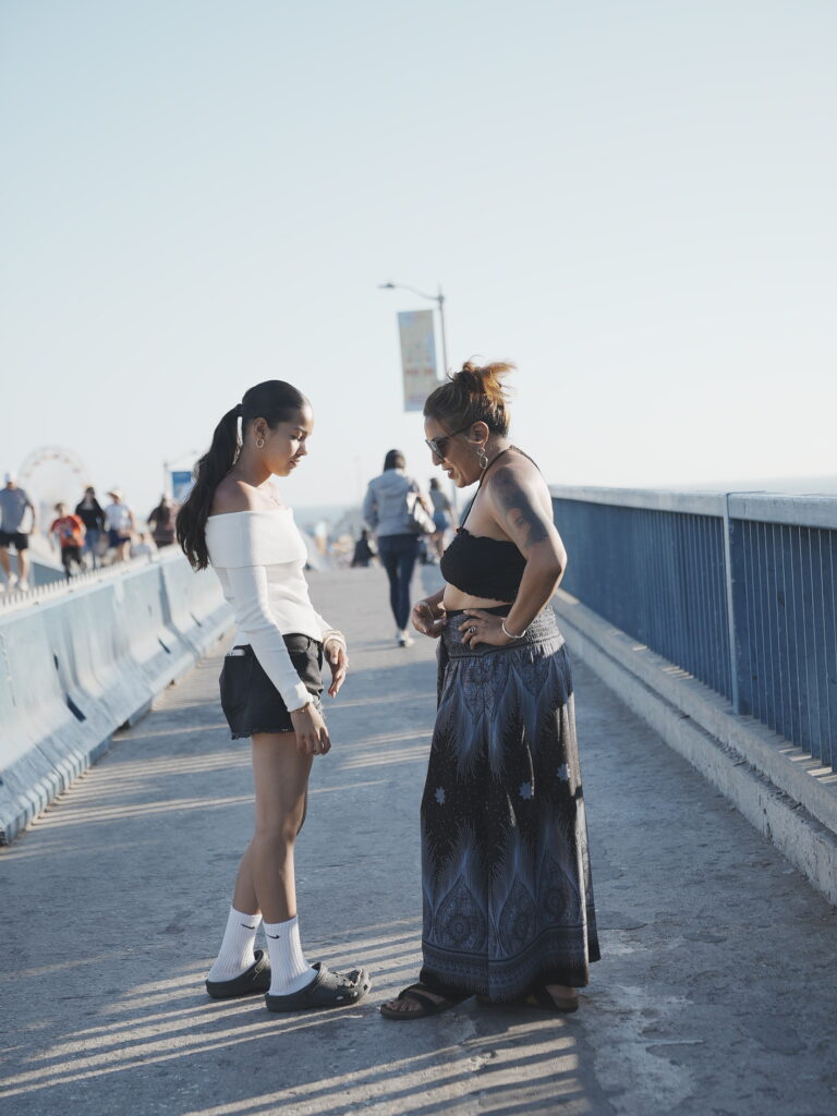 Mother and daughter standing together on Santa Monica Pier during golden hour, sharing a quiet moment with the ocean breeze and warm sunlight.